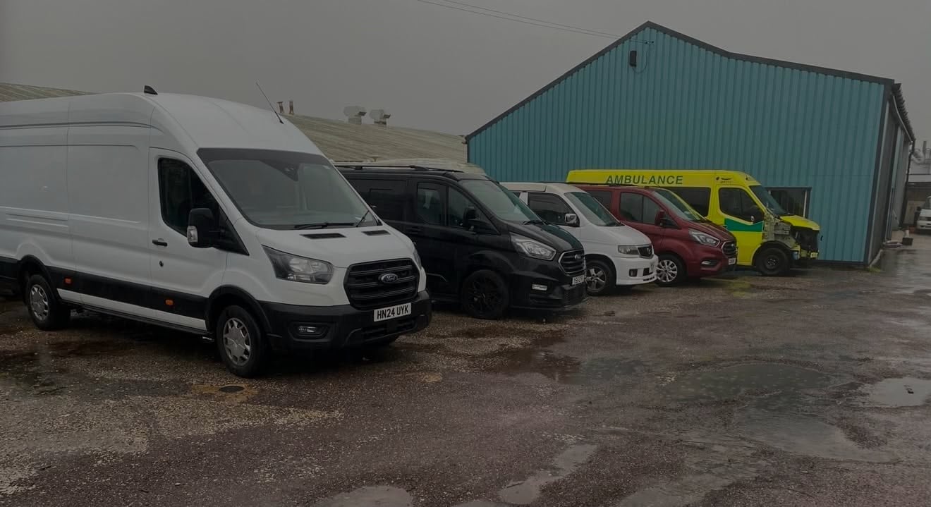 Row of parked service and utility vehicles in front of a green metal warehouse building on a wet pavement