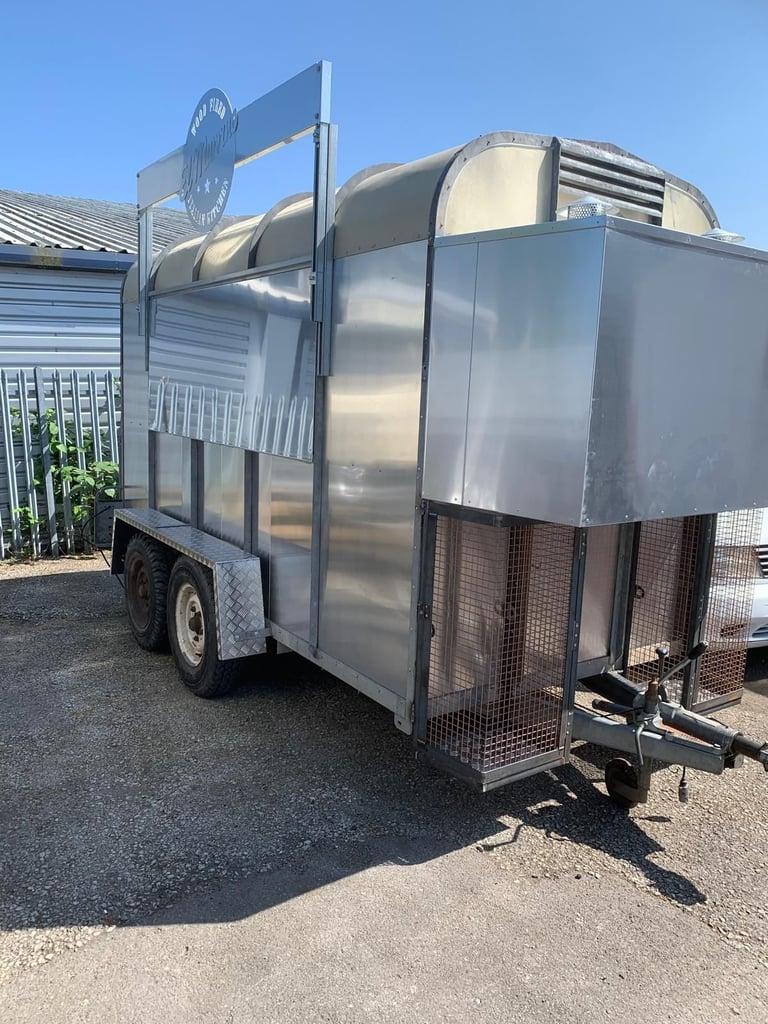 Aluminum livestock trailer with dual axles, ventilation panels, and rear ramp doors parked outdoors